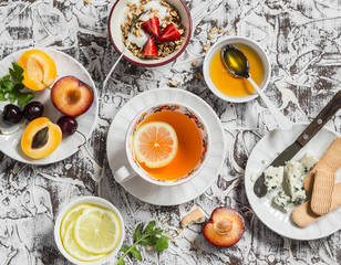 Breakfast or snack table. Lemon tea, fresh fruit, yogurt with granola, blue cheese, biscuits. On a light background