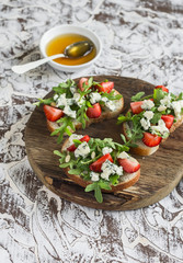 Sandwiches with strawberries, arugula and blue cheese on rustic wooden board on light background. Delicious snack, breakfast or  appetizer with wine