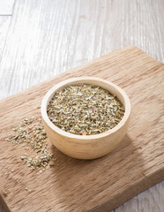 Dried oregano leaves in wooden bowl on chopping board