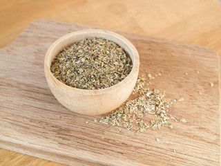 Dried oregano leaves in wooden bowl on chopping board