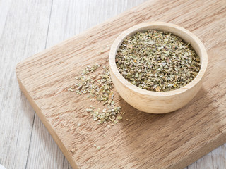 Dried oregano leaves in wooden bowl on chopping board