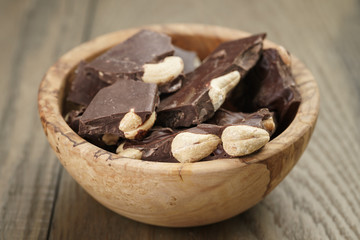 broken homemade bar of chocolate with cashew nuts in wood bowl