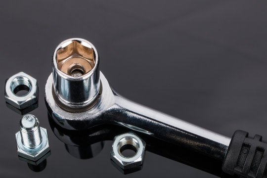 Ratsche, Schraubenschl&uuml;ssel und Schrauben auf schwarzem spiegelndem Hintergrund