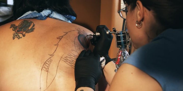 Tattoo artist chatting as she inks and wipes a design on a customer's back