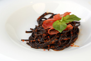 White plate of black spaghetti with red souse and greens