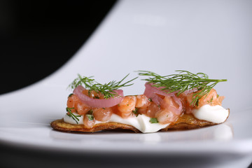 Appetizer on fried potato skins of red salted salmon, cream cheese, onions and dill at white plate. Closeup