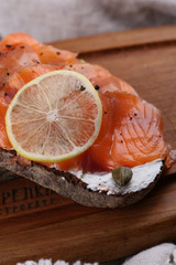 Bread with salmon, cream cheese and lemon on a wooden board, selective focus.