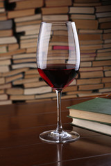 Glass of red wine on wooden table against backdrop the books