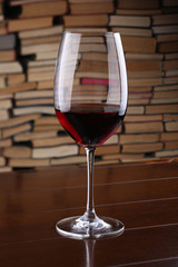 Glass of red wine on wooden table against backdrop the books
