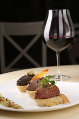 Assortment of pate canapes bread on white plate with glass red wine, dark background
