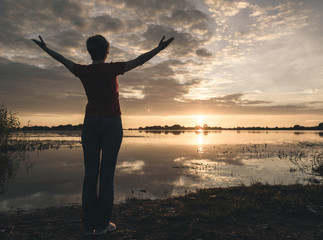 Fototapeta premium young slim woman meditating onbanks of the lake at sunset