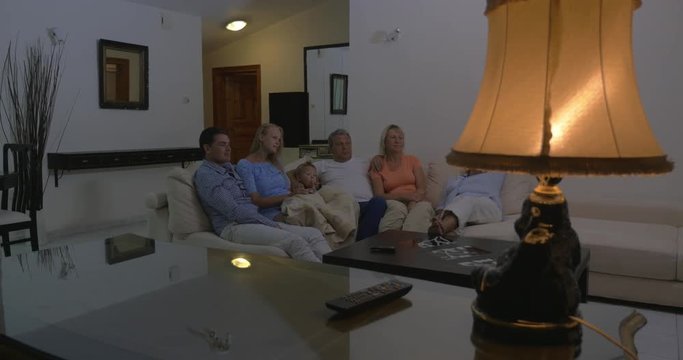 Big family with parents, child and grandparents spending evening time on watching TV. They sitting together on the sofa at home