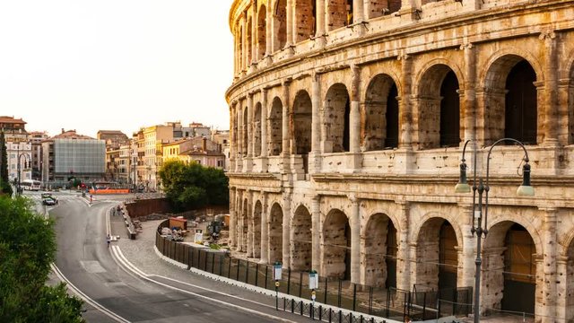 Time-lapse in Rome, Italy. Morning in the city. Sunrise over the Colosseum - famous landmark in country. Occasional buses and people running and walking in the road, crawling sunlight