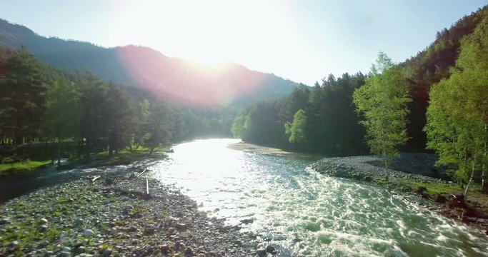 4k (UHD) aerial view. Low flight over fresh cold mountain river at sunny summer morning. Green trees and sun rays.