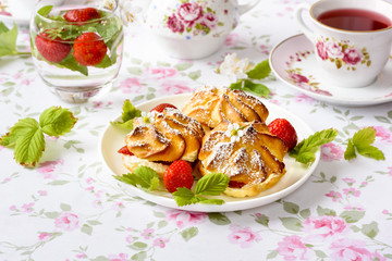 Cream puffs or profiterole filled with whipped cream, powdered sugar topping served with strawberries on the table