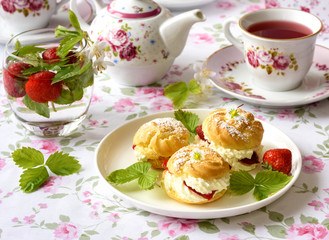 Cream puffs or profiterole filled with whipped cream, powdered sugar topping served with strawberries on the table
