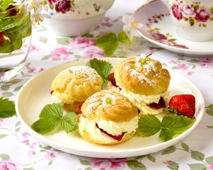 Cream puffs or profiterole filled with whipped cream, powdered sugar topping served with strawberries on the table