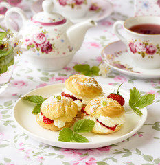 Cream puffs or profiterole filled with whipped cream, powdered sugar topping served with strawberries on the table