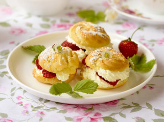 Cream puffs or profiterole filled with whipped cream, powdered sugar topping served with strawberries on the table