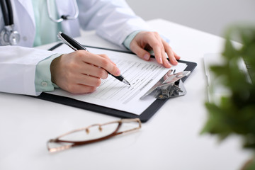 Fototapeta premium Close-up of a female doctor filling out application form , sitting at the table in the hospital