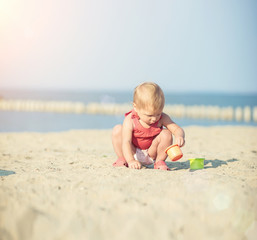 Baby playing on the sandy beach near the sea. Cute little girl in red dress with sand on tropical beach. Ocean coast.