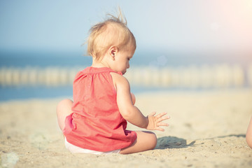Fototapeta na wymiar Baby playing on the sandy beach near the sea. Cute little girl in red dress with sand on tropical beach. Ocean coast.