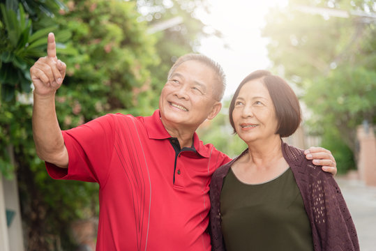 Happy senior Asain couple outdoor with man pointing into distance.Warm tone photo with sunlight.