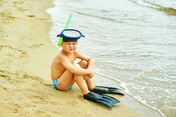 little boy posing on the beach wearing snorkeling equipment. On the background of the sea