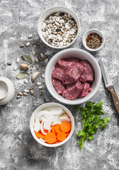 Raw ingredients - beef, beans, onions, carrots, spices and herbs, tomato sauce on a light stone background