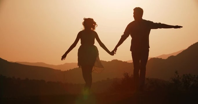 couple silhouette running forward holding hands with the sunset Golden hour, the sun a warm color, slow motion