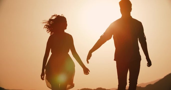 couple silhouette walking in the highlands holding hands with the sunset Golden hour, the sun a warm color, slow motion
