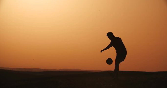 football player silhouette , practicing with the ball,the sunset Golden hour, slow motion