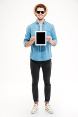 Smiling handsome young man standing and holding blank screen tablet