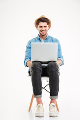 Smiling man in hat sitting on chair and using laptop