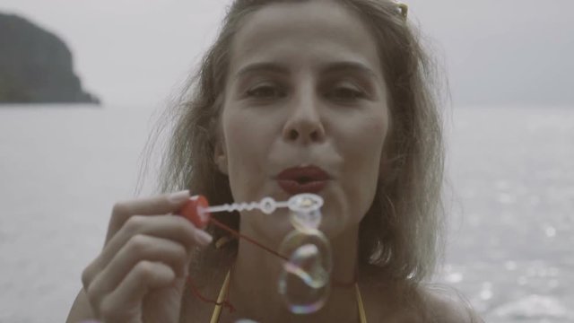 Pretty young happy woman wearing bikini doing soap bubbles during her holiday with beatiful view behind in slow motion.