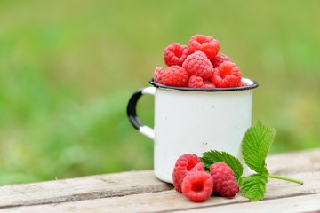 Fresh red raspberries in mug on wooden background