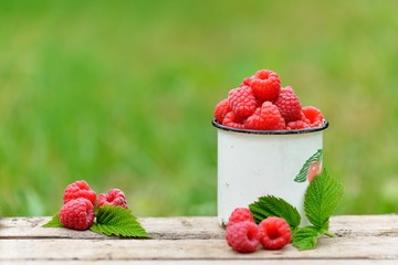 Fresh red raspberries in mug on wooden background