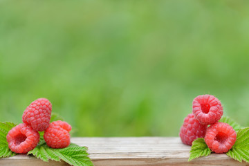 Fresh red raspberries on wooden table on blurred natural background