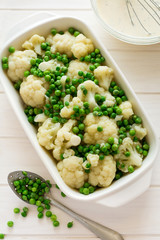 Cooking cauliflower and peas gratin in a baking tin on white wooden background