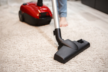 Maid cleaning carpet with modern red vacuum cleaner