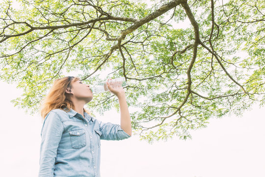 young beautiful  woman drinking water at summer green park.