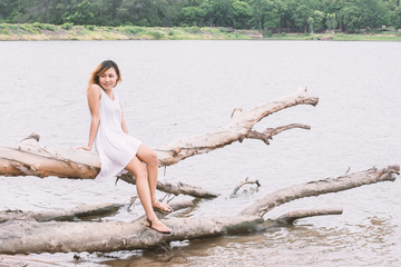 Young woman sitting on tree trunk at lake and smiling.