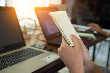 Note book in hand people are working with computers on wooden ta