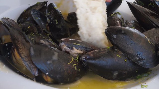 An ultra closeup POV shot of foodie dipping toasted bread on fresh mussels with butter sauce
