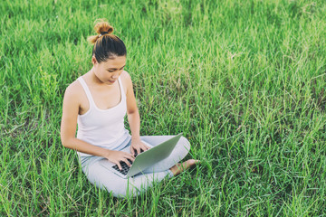 Naklejka na ściany i meble Young woman with laptop sitting on green grass at meadows.