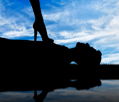 Silhouette feminists legs standing on the prone man and a reflection in water