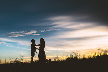 Mother encouraged her son outdoors at sunset, silhouette concept