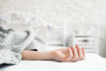 Hand of sleeping in bed covered woman closeup. Focus on female hand with french manicure, bedroom interior on background. Relaxed female hand. Illness First Aid Suicide Death Heart Rate Concept