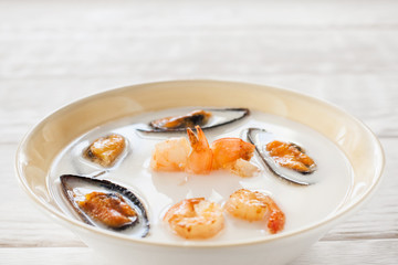 Cream-soup with shrimps and mussels copyspace. Bowl with seafood cream-soup on white wooden background. White soup with mussels and shrimps in bowl