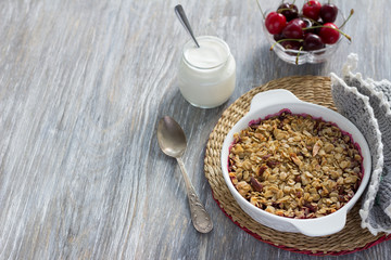 Homemade cherry crumble with oatmeal and almonds with fresh cherry and yogurt on a light wooden table 